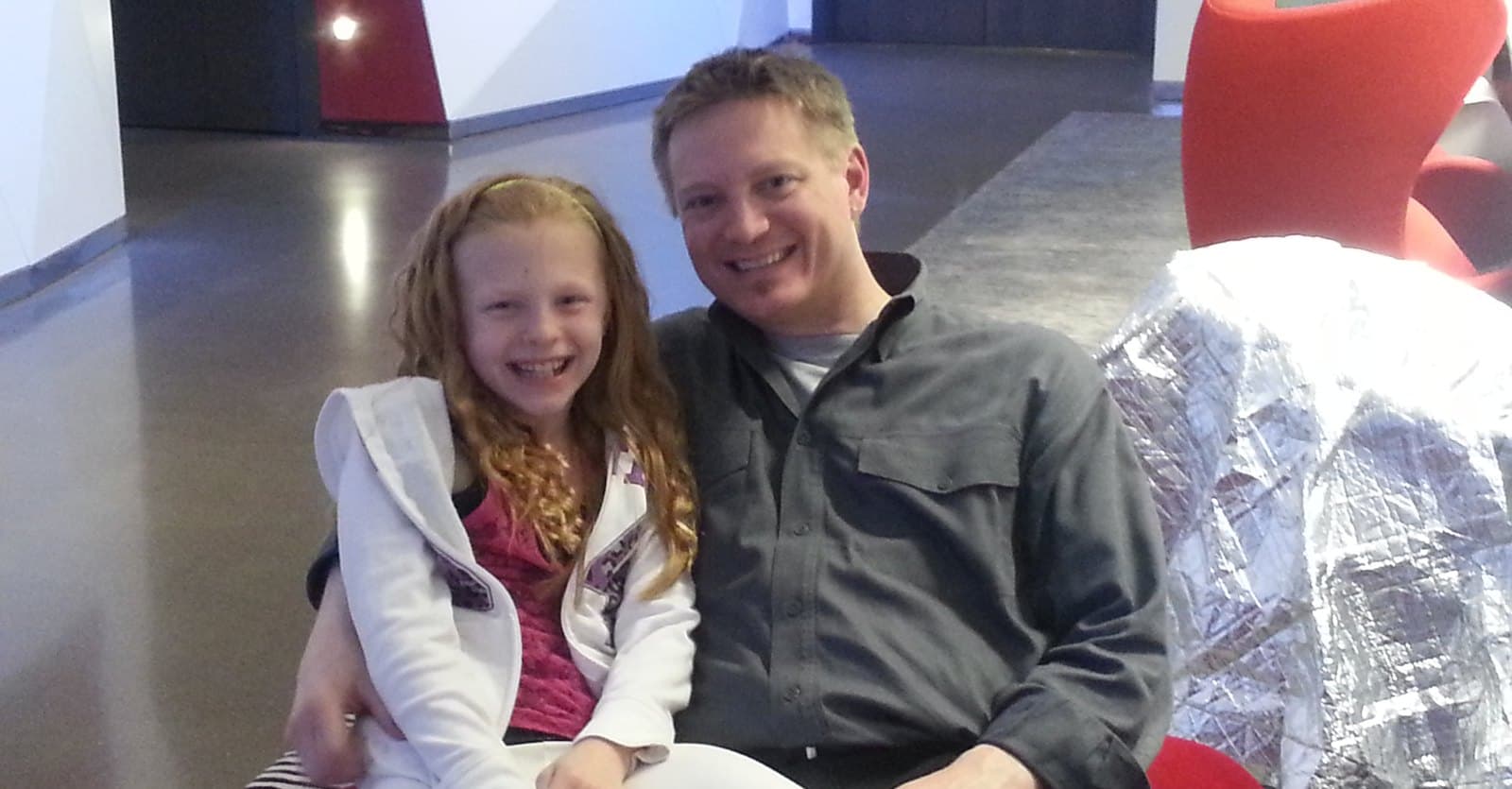 Rich and his daughter, about nine years old, sitting together on a bench and smiling at the camera